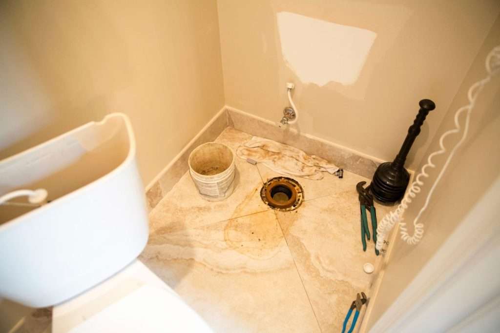 Sewage cleanup work in a bathroom with exposed drain and cleanup tools